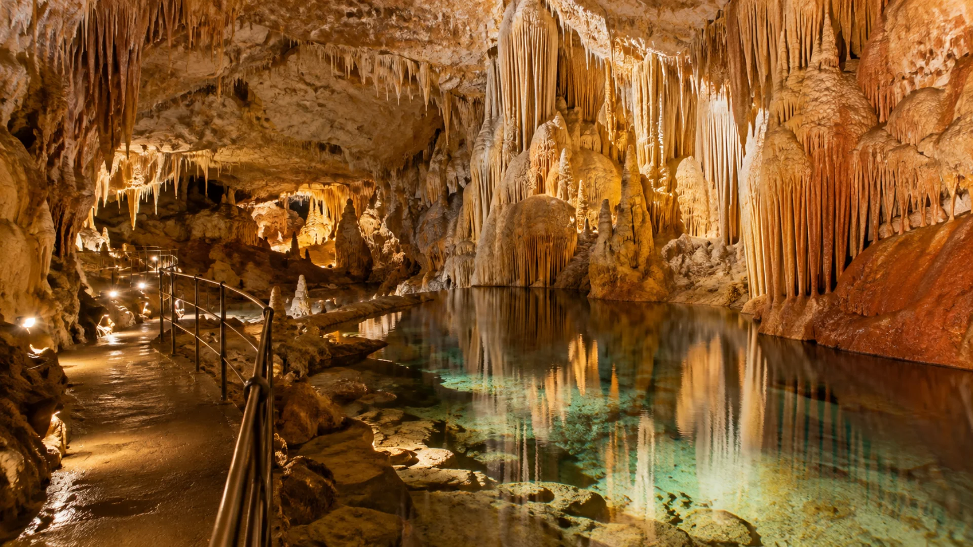 Sala sotterranea con stalattiti bianche, gialle e rosse che si riflettono in un laghetto immobile nelle Grotte di Borgio Verezzi